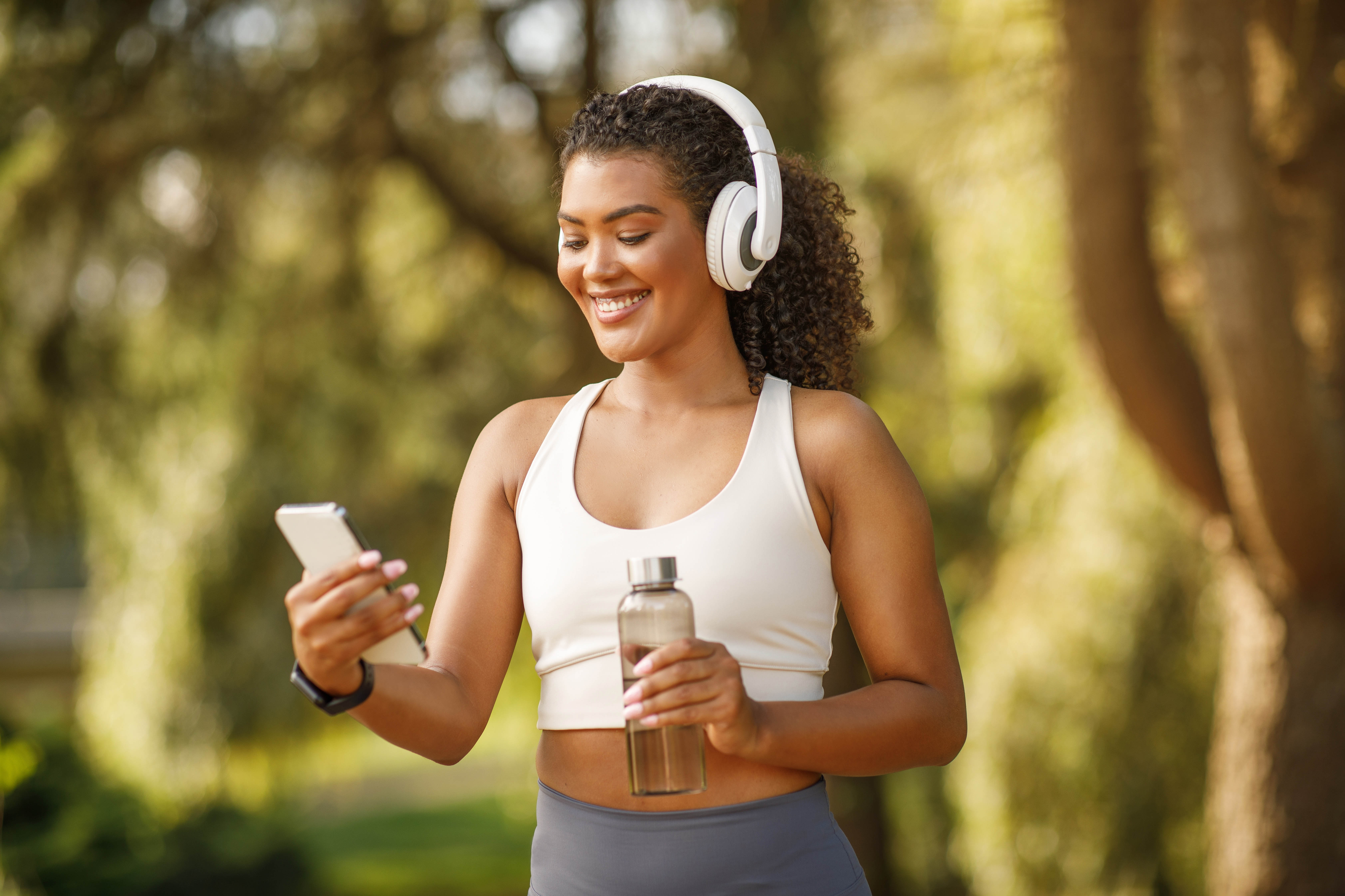 Young woman outside with her headphones on, smiling at her phone doing an outdoor workout Young woman outside with her headphones on, smiling at her phone doing an outdoor workout